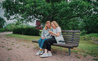 Tytöt istuvat Myllymäen puiston penkillä.Taustalla näkyy mylly.