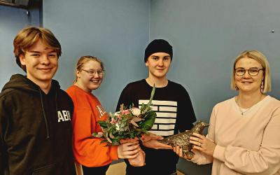kolme nuorisovaltuustolaista ojentaa kukkia ja naakkapatsasta Jennika Saloselle