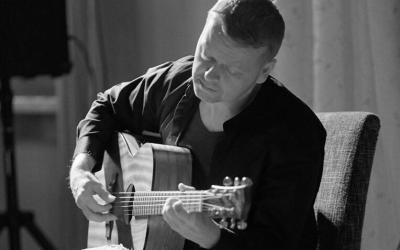 Mustavalkoinen kuva, jossa Tomi Paldanius istuu soittamassa kitaraa