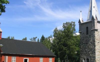 Punaiseksi maalattu, vanha puinen uhrikirkko ja uudempi harmaakivinen kirkko
