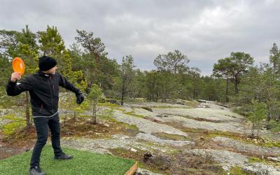 mies heittää frisbeetä kallioisella metsäkummulla