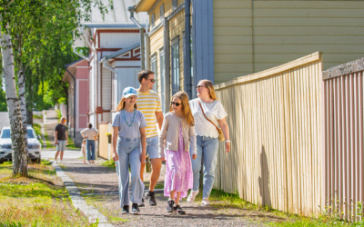 Nainen, mies ja kaksi tyttöä kävelee puutalokeskustassa kauniina kesäpäivänä.