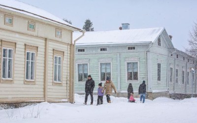 Ihmisiä kävelee lumisella kadulla talvipäivänä, taustalla puutaloja.
