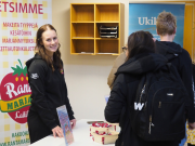 Nainen katsoo kameraan ja hymyilee. Hänen edessä on pari nuorta.