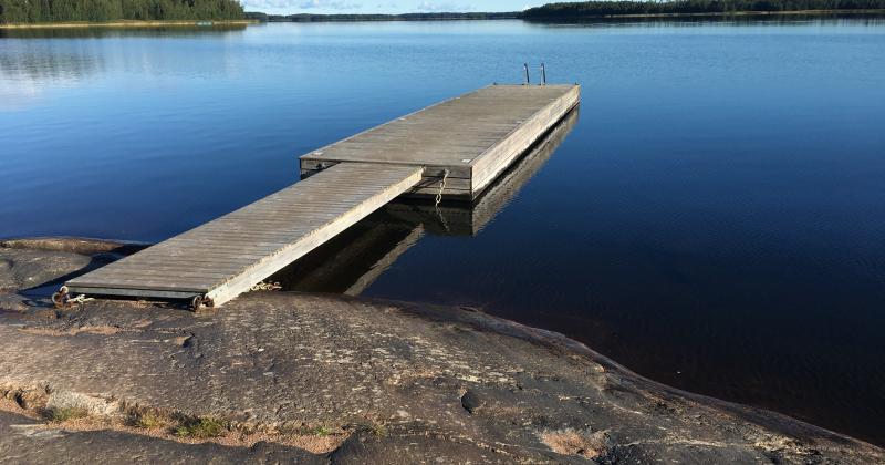 Kalliolta alkava laituri siniselle järvelle, takana siintää puita