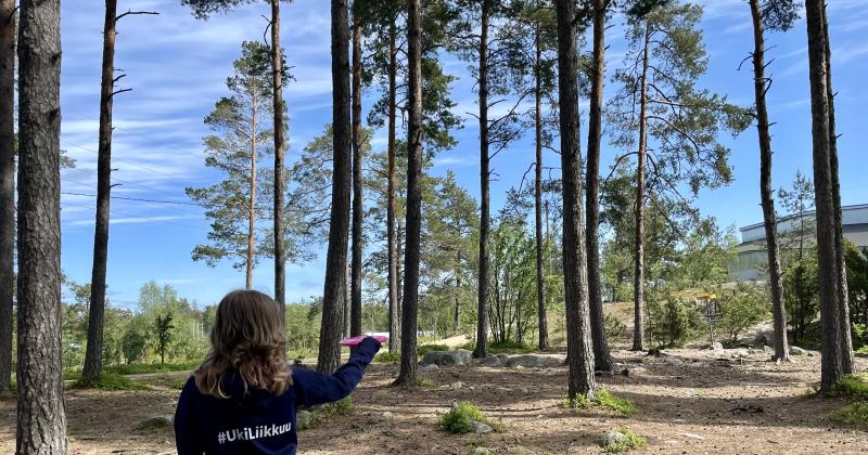 Tyttö heittää frisbeetä metsäisellä radalla