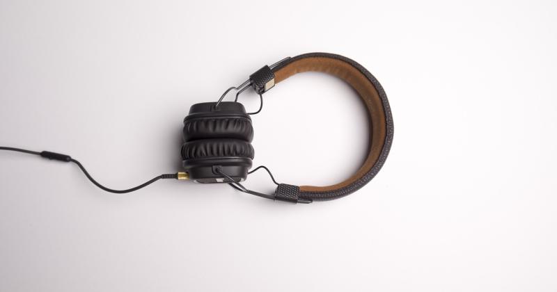 Vanhanaikaiset kuulokkeet lepäävät pöydällä. Kuulokkeet ovat mustat ja tummanruskeat. Kuulokkeista lähtee johto, mikä ulottuu kuvan ulkopuolelle vasemmalle.