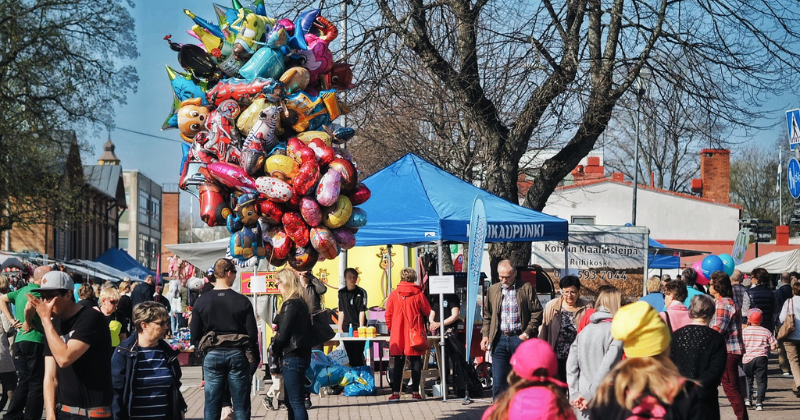 Paljon ihmisiä ja markkinakatoksia torilla, sekä iso rykelmä heliumilmapalloja leijumassa ilmassa.