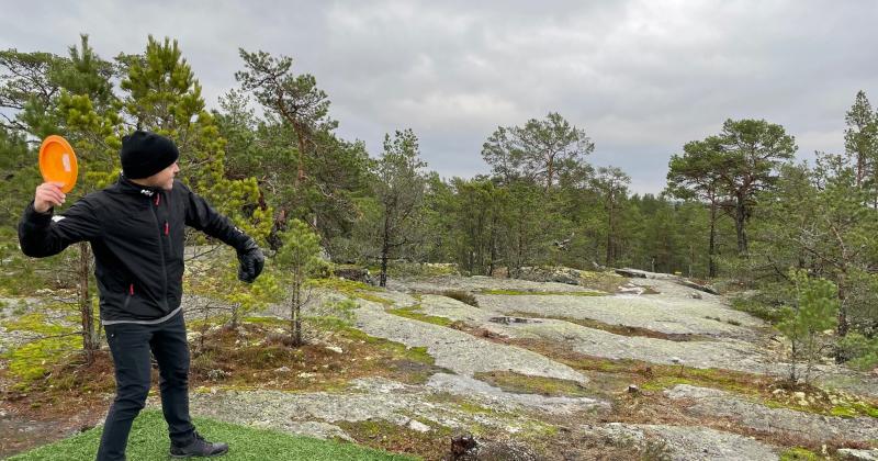 mies heittää frisbeetä kallioisella metsäkummulla