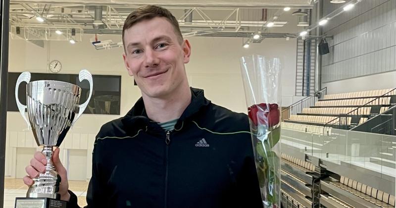 mies pitelee pokaalia ja ruusua, taustalla liikuntahalli