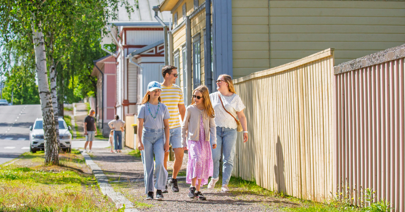 Nainen, mies ja kaksi tyttöä kävelee puutalokeskustassa kauniina kesäpäivänä.