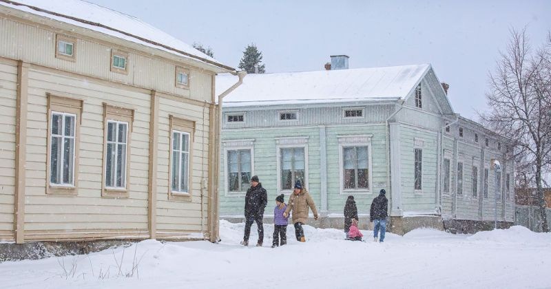Ihmisiä kävelee lumisella kadulla talvipäivänä, taustalla puutaloja.