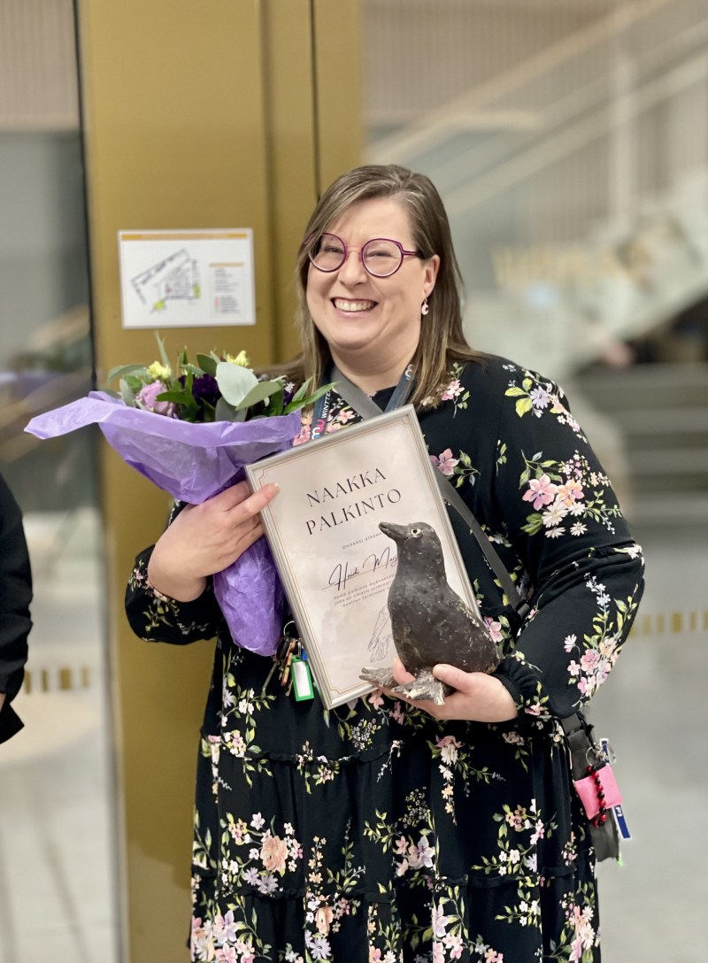 nainen poseeraa naakka-palkinnon, kukkasten ja kunniakirjan kera