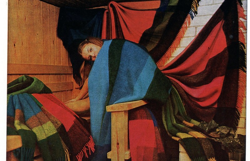 Nainen värikkäiden vilttien kanssa saunassa.